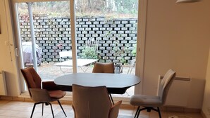 Ein Essbereich mit einem runden Tisch und vier Stühlen, einem großen Fenster mit Blick auf eine Ziegelwand und Grünpflanzen sowie einem Deckenventilator.