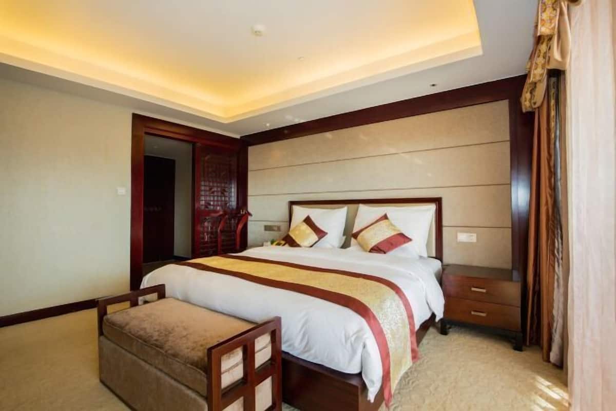 A hotel room with a large bed, a wooden nightstand, a bench, and a wardrobe.