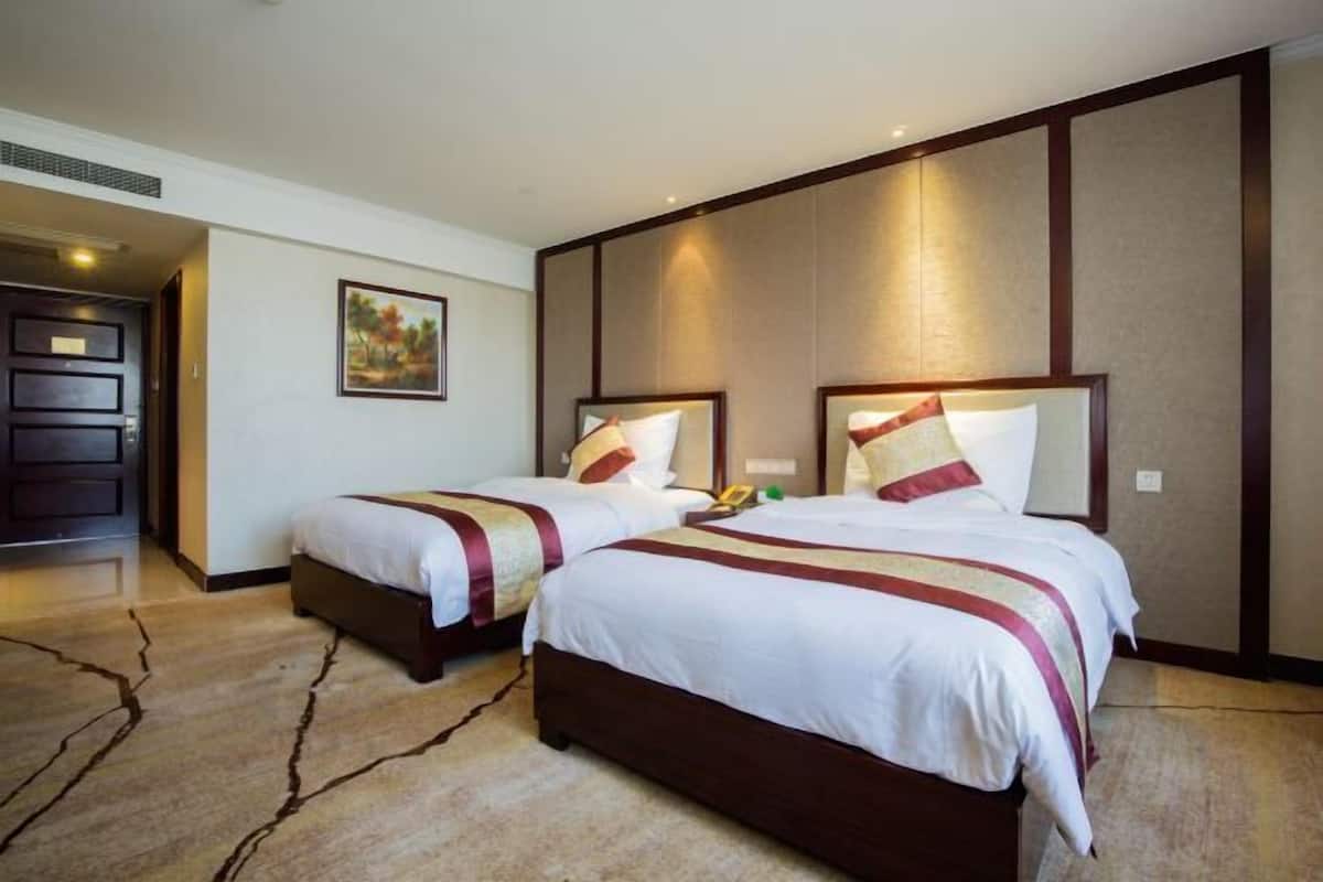 A hotel room with two beds, a large painting on the wall, and a door leading to another room.