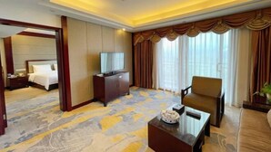 Une chambre d’hôtel comprenant un lit, une télévision, un canapé, une table basse et une grande fenêtre avec des rideaux.