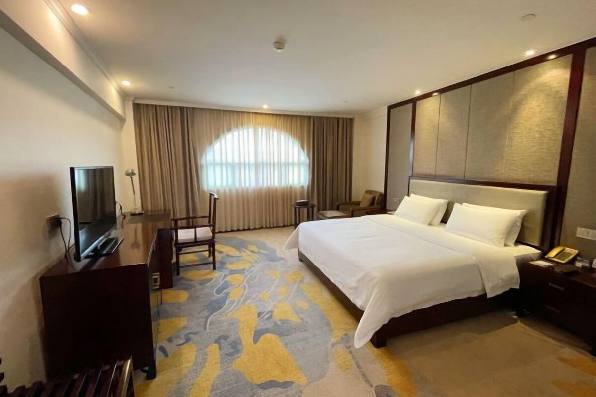 A hotel room with a bed, a desk, a chair, a television, and a large window with curtains.
