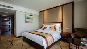 A hotel room with a large bed, a wooden nightstand, a chair, and a small table. - XINFANDIAN Hotel (Ganzhou)