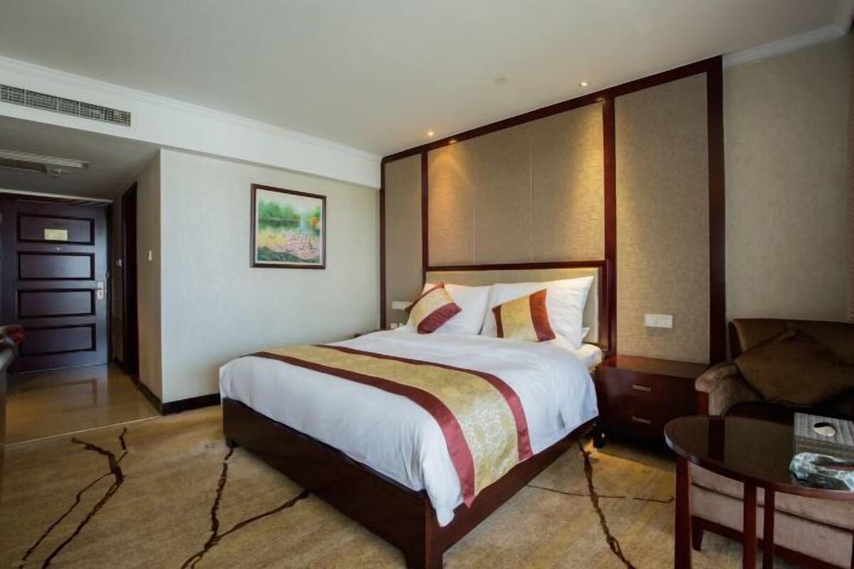 A hotel room with a large bed, a wooden nightstand, a chair, and a small table.