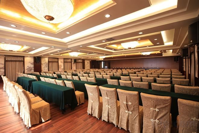 A conference room with rows of tables and chairs, a chandelier, and a stage.