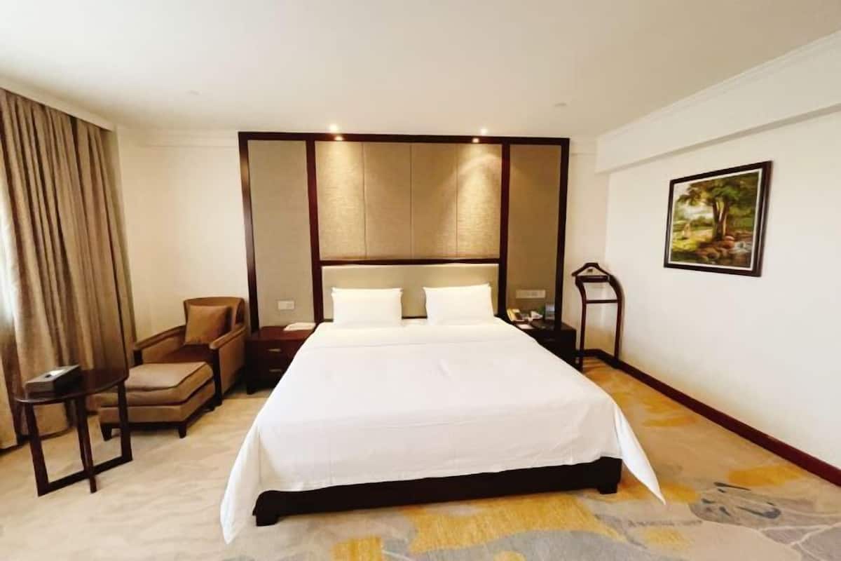 A hotel room with a large bed, a chair, a small table, and a painting on the wall.