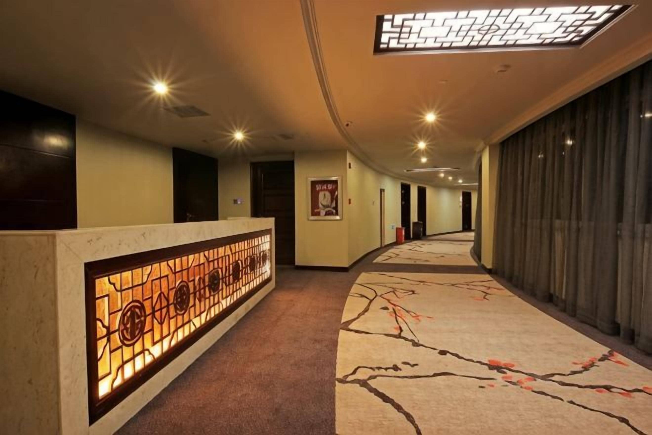 A hotel corridor with a reception desk, a patterned carpet, and a ceiling with recessed lighting.