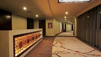 A hotel corridor with a reception desk, a patterned carpet, and a ceiling with recessed lighting.