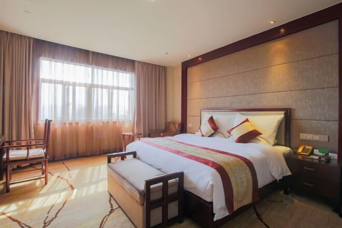 A hotel room with a large bed, a bedside table, a chair, and a window with curtains.
