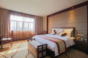 Habitación de hotel con una cama grande, una mesita de noche, una silla y un ventanal con cortinas.