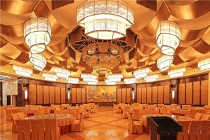 A large banquet hall with round tables and chairs, chandeliers, and a mural on the back wall. - XINFANDIAN Hotel (Ganzhou)