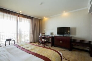A hotel room with a bed, a desk, a chair, a television, and a balcony with curtains.