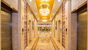 Un hall d’hôtel avec un sol en marbre, des lustres, des ascenseurs et un comptoir d’accueil.
