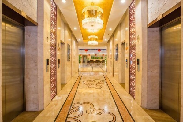 A hotel lobby with a marble floor, chandeliers, elevators, and a reception area. - XINFANDIAN Hotel (Ganzhou)