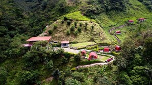 An aerial view of a rural property with several red-roofed buildings, a central structure with a red roof, and lush green vegetation. - Termales El Escondite (Samaná)