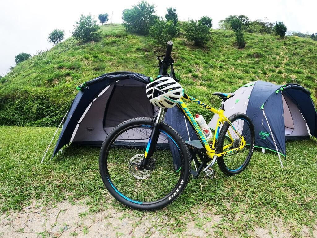 Un vélo est garé à côté d’une tente sur une colline herbeuse.