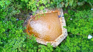 A square-shaped water feature surrounded by lush greenery. - Termales El Escondite (Samaná)