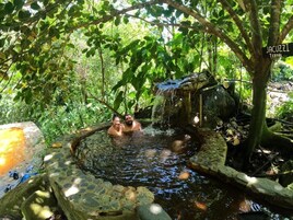 Una fuente termal natural rodeada de vegetación exuberante y una estructura de piedra.