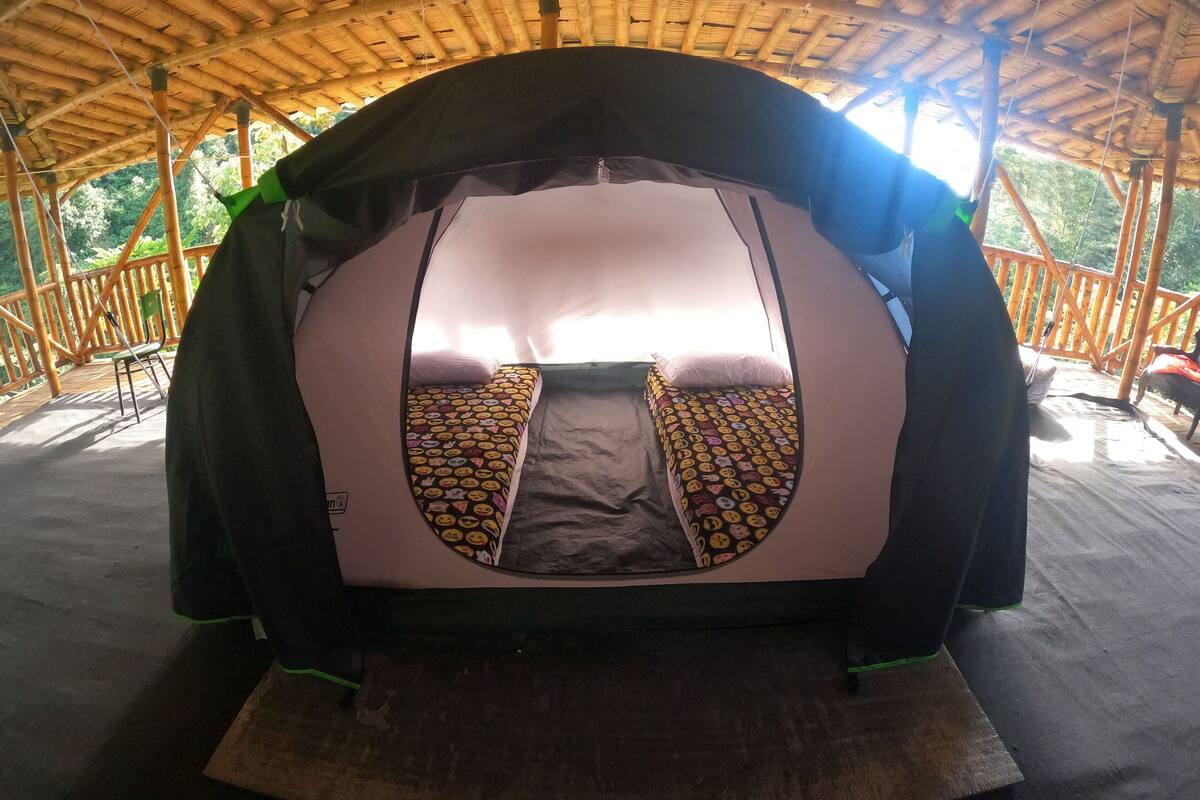 A tent with a bed inside, surrounded by a wooden structure with a thatched roof.