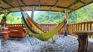 A hammock under a wooden roof, stone flooring, and a view of lush greenery. - Termales El Escondite (Samaná)