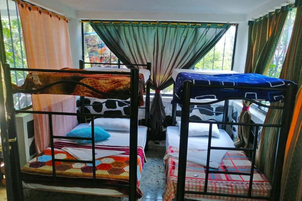 A room with two bunk beds, each with a colorful quilt. There are curtains on the windows, and the room has a tiled floor.