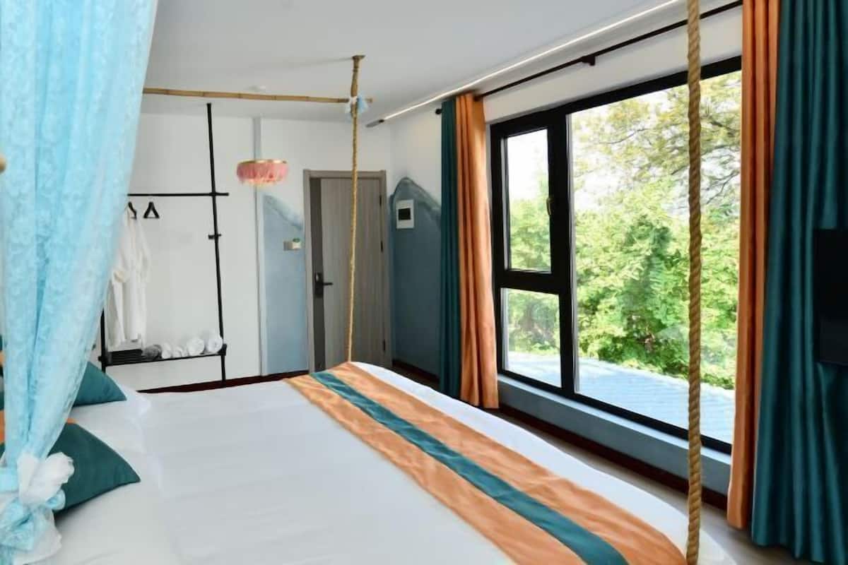 Ein Schlafzimmer mit Bett, Vorhängen, einem Fenster und Blick auf Grünflächen.