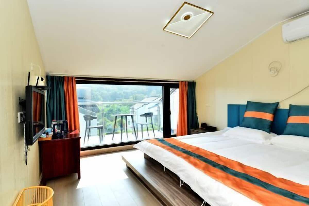 Ein Hotelzimmer mit einem großen Bett, einem Fernseher, einem Schreibtisch und Blick ins Freie.