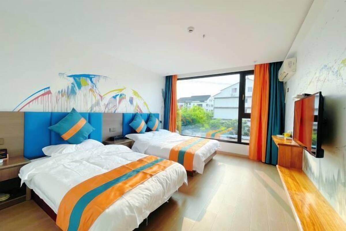 Ein Hotelzimmer mit zwei Betten, einem großen Fenster, einem Fernseher und einem Gemälde an der Wand.