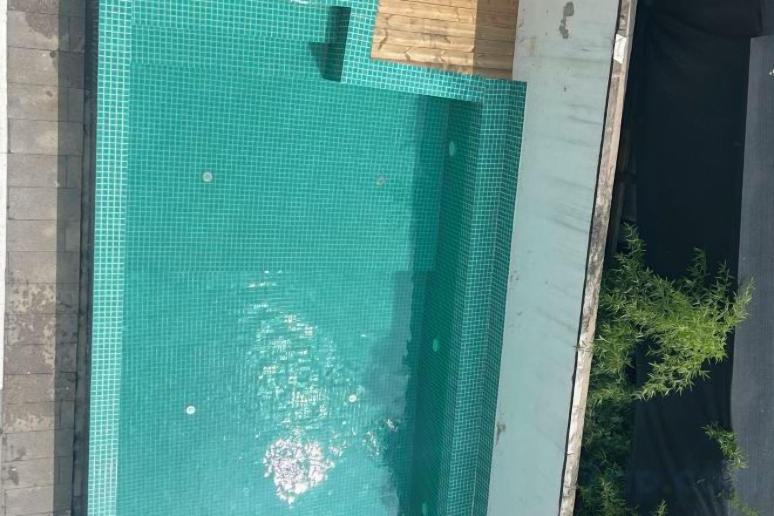 A swimming pool with a tiled surface, surrounded by a concrete edge and a wooden deck.