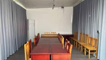 Un salón de conferencias con una larga mesa y sillas, una pizarra y cortinas.