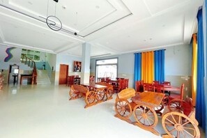 A spacious hotel lobby with a central seating area featuring wooden tables and chairs, a staircase, and a large window. - Sanshan Island Bee Cai Homestay (Suzhou)