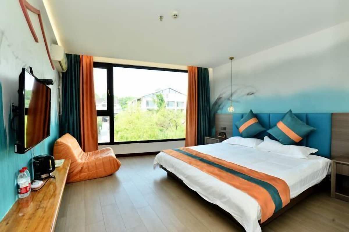 Ein Hotelzimmer mit Bett, Schreibtisch, Stuhl, Fernseher und einem Fenster mit Vorhängen.