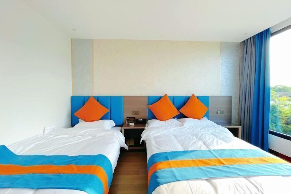 Habitación de hotel con dos camas, una mesita de noche y una ventana con cortinas.