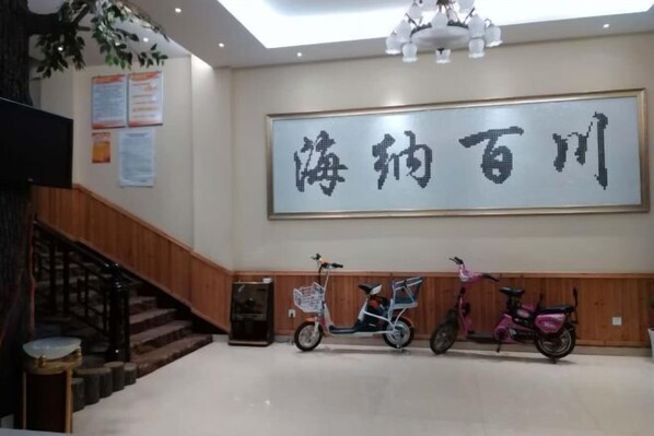 A spacious lobby with a staircase, a large wall-mounted sign, and two scooters parked against the wall.