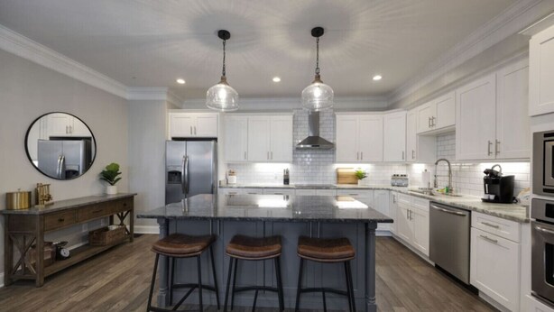 A modern kitchen with a central island, bar stools, stainless steel appliances, and pendant lighting.