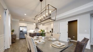 A modern dining area with a long table, chairs, and a hanging light fixture.