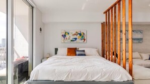 Una camera da letto moderna con un letto grande, una testiera in legno e vista sulla città attraverso una porta scorrevole.