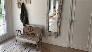 Ein Zimmer mit einer hölzernen Bank mit dem Schriftzug 'TOUTON', einem rustikalen Spiegel und einem Kleiderständer mit Hüten.