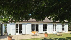 Ein weißes Gebäude mit Fensterläden, einer Terrasse mit Sitzgelegenheiten und Topfpflanzen.
