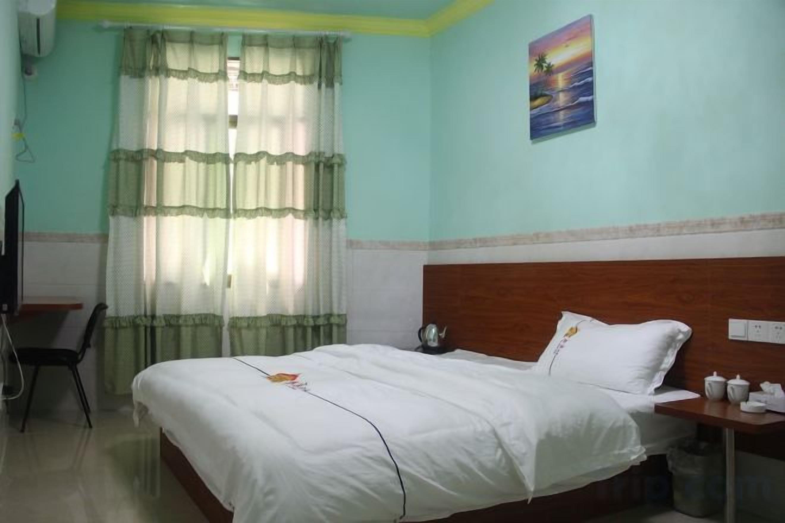 A hotel room with a bed, a desk, a chair, a window with curtains, and a wall-mounted television.
