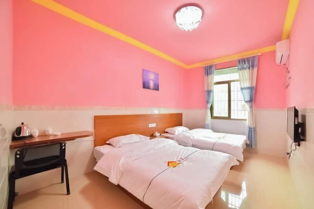 A room with pink walls, a wooden headboard, two beds with white bedding, a small table with a kettle, a picture on the wall, and a window with curtains.