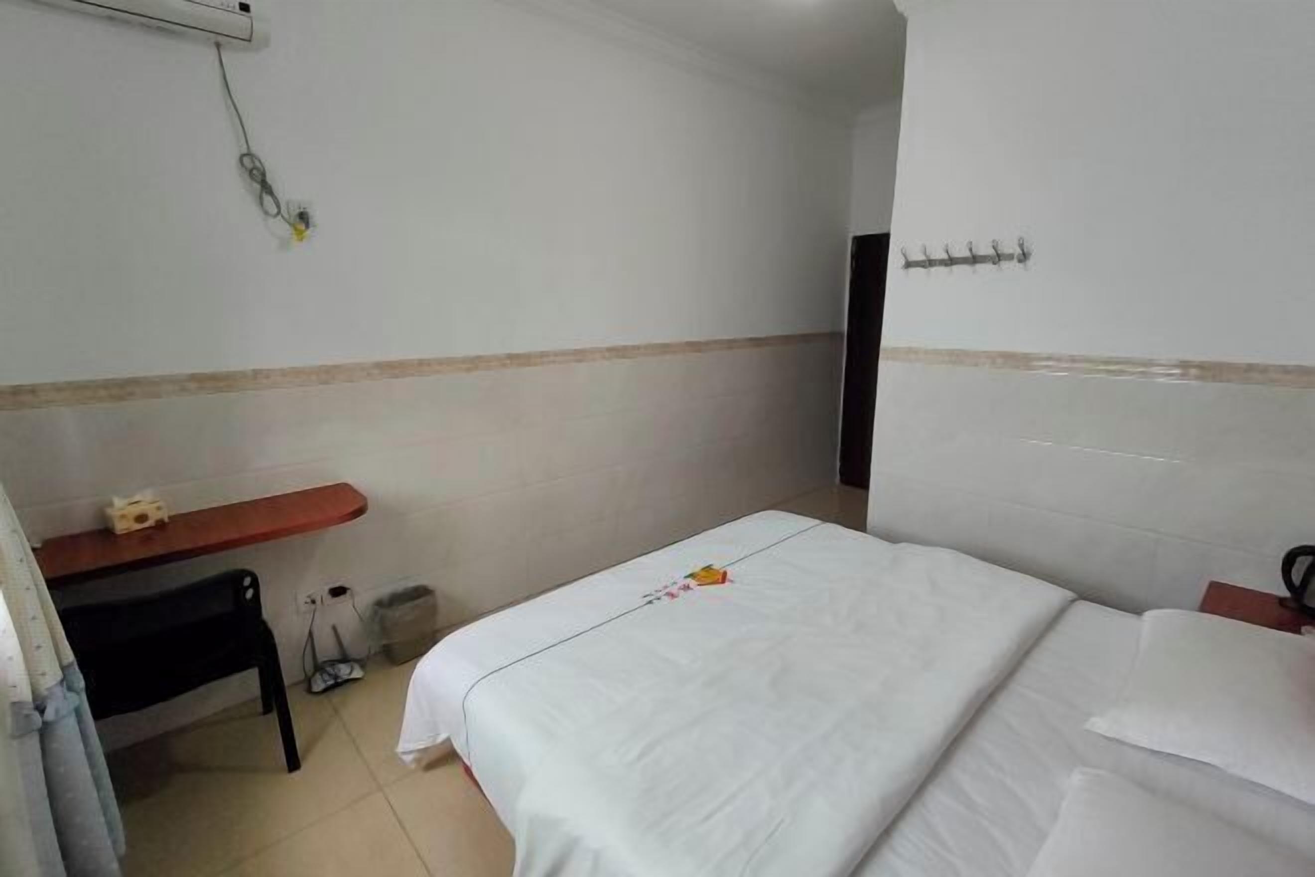 Camera d'albergo con un letto, una scrivania, una sedia, un cestino e un gancio a parete.
