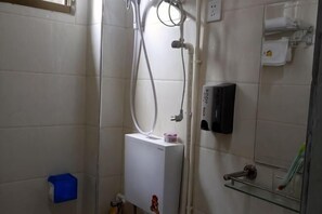 A bathroom with a white tiled wall, a white heater, a glass shelf with toiletries, and a blue trash bin.