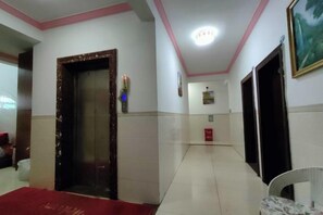 Un pasillo de hotel con alfombra roja, una puerta, una lámpara fijada a la pared y un cuadro enmarcado.