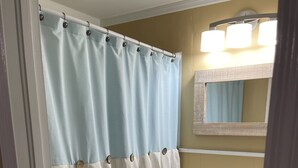 Un baño con cortina de ducha, lavabo, espejo y armarios de madera.
