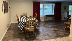 Un comedor con una mesa lista para dos, sillas de madera, una mesita auxiliar y una ventana con persianas.