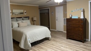 Un dormitorio con una cama, un aparador, un ventilador de techo, una puerta y una pared decorada con un letrero.