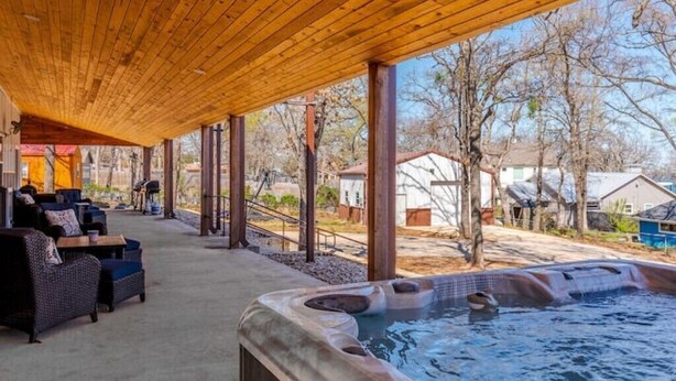 A covered outdoor area with a hot tub, seating, and a view of the surrounding neighborhood.