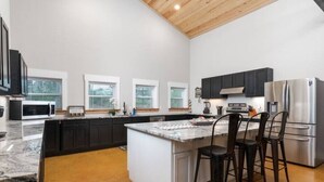 A modern kitchen with dark cabinets, a stainless steel refrigerator, and a marble countertop.