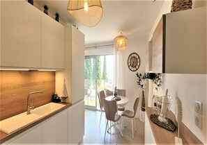 Eine moderne Küche mit eingebautem Spülbecken, eine Essecke mit rundem Tisch und Stühlen sowie Blick ins Freie.