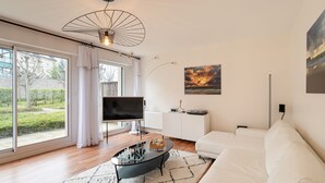 A modern living room with a large window, a flat-screen TV, a white sofa, and a coffee table with a chess set. - La Petite Maison Dans la Prairie - Havre de paix (Rennes)